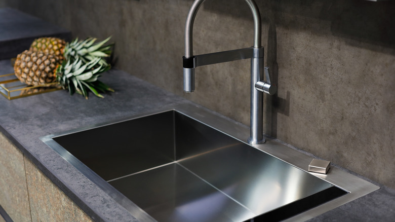 Closeup of stone countertop with stainless steel sink and pineapples in background.