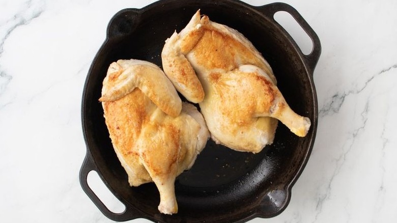 Seared whole chicken halves in cast iron skillet