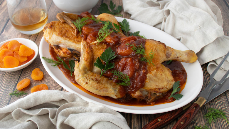 chicken in a reddish-brown sauce with green herbs on a white plate