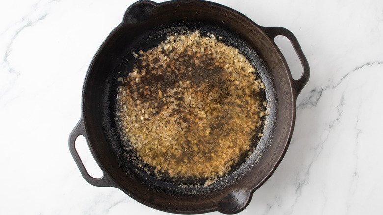 brown liquid with chopped onions in a black frying pan