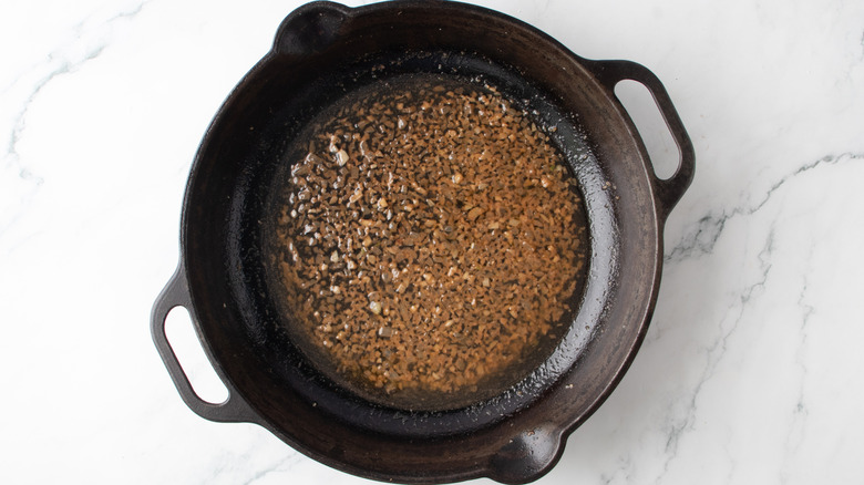 brown liquid with chopped onions in a black frying pan