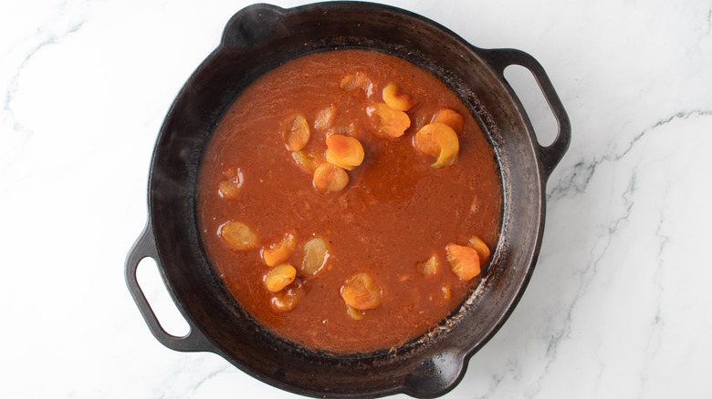 reddish-brown liquid and dried apricots in a black frying pan