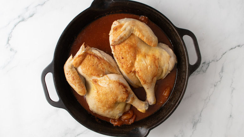 chicken in reddish-brown liquid in a black frying pan