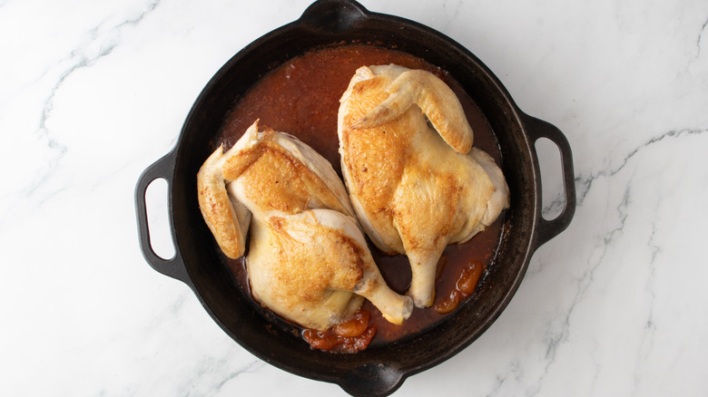 chicken in reddish-brown liquid in a black frying pan
