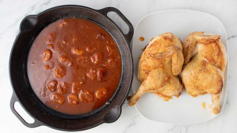 chicken next to reddish-brown liquid in a black frying pan