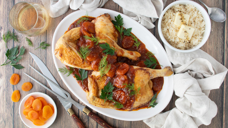 chicken in a reddish-brown sauce with green herbs on a white plate