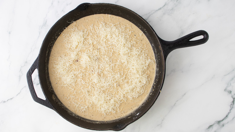orangish creamy liquid and parmesan cheese in a black frying pan