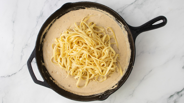 orangish creamy liquid and  noodles  in a black frying pan