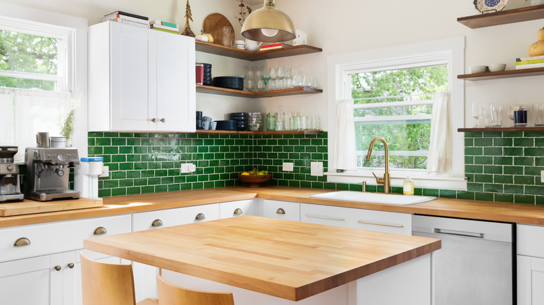 An otherwise stylish kitchen with green tile backsplash has outdated butcher block countertops.