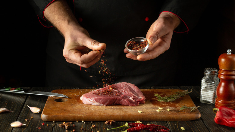 chef sprinkles spices on a steak
