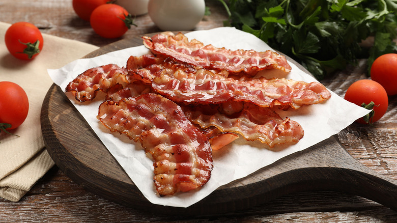 cooked slices of bacon on parchment paper on wooden tray