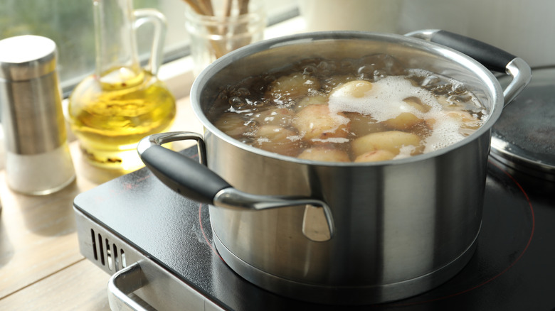 A big pot of potatoes boils on the stove in natural light.