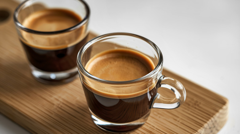 Two separate shots of espresso in a with a nice layer of crema, set atop a wooden board.