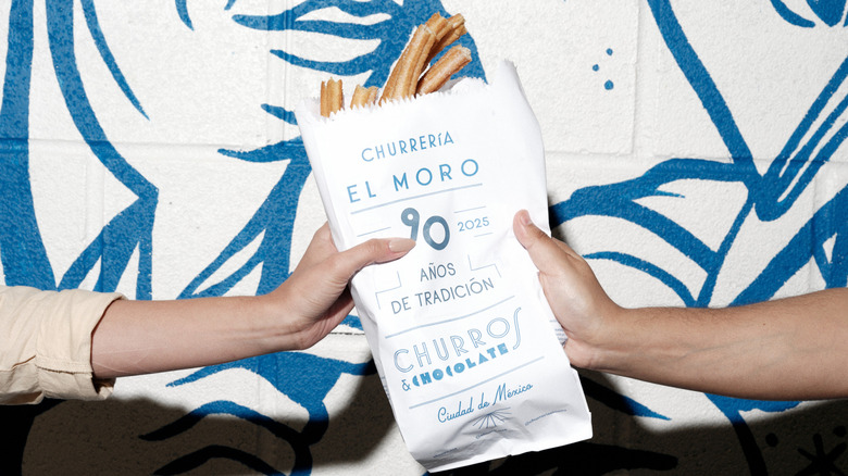 A person handing off a bag of churros to another