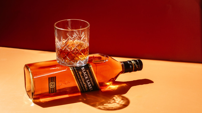 A glass of Johnnie Walker whisky sits atop a bottle of Johnnie Walker Black Label