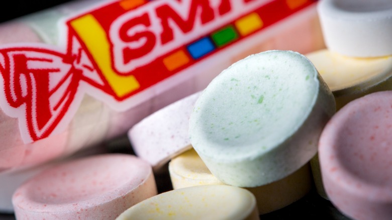 Assorted pieces of Smarties candy sitting next to a wrapped tube of Smarties.