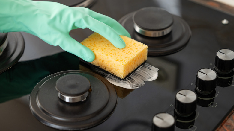 A gloved hand cleaning a gas oven stovetop.