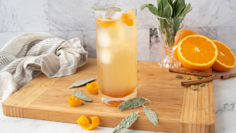 pale, orange-colored cocktail in a tall glass with ice and orange peels