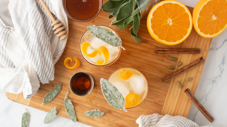 pale, orange-colored cocktails with ice, sage leaves, and orange peels