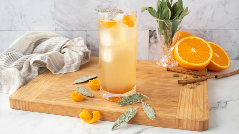 pale, orange-colored cocktail in a tall glass with ice and orange peels