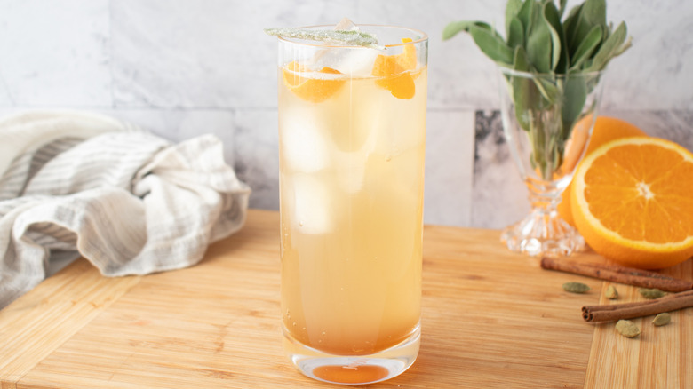 pale, orange-colored cocktail in a tall glass with ice and orange peels