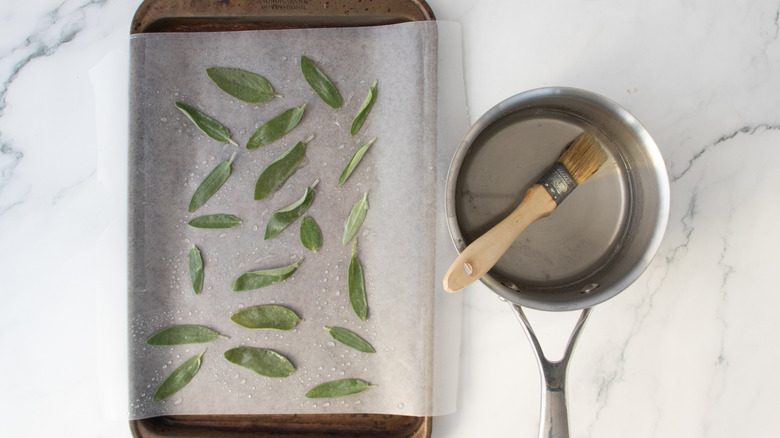 sage leaves on wax paper next to a pot with a paintbrush