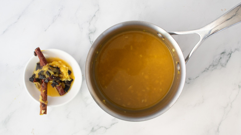 orange juice in a metal pot next to a strainer full of spices