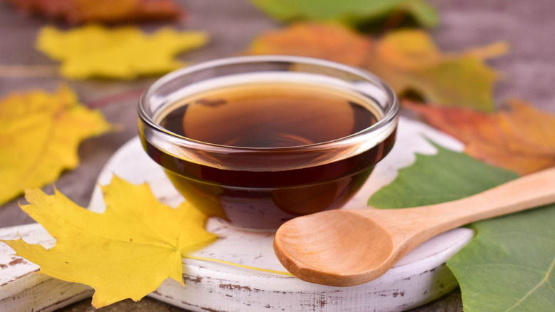 A bowl of maple syrup with wood spoon surrounded by maple leaves.