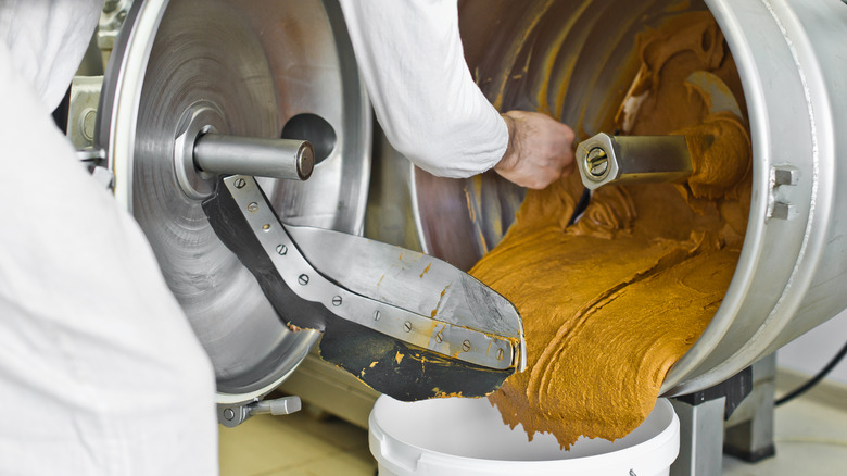 Person making peanut butter in a large metal machine