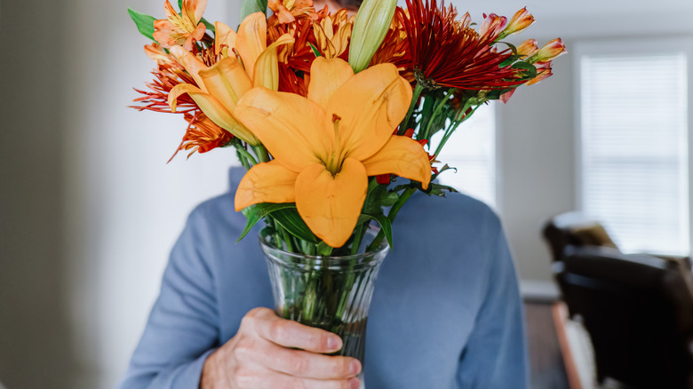 Man holds a vase of flowers in front of his face
