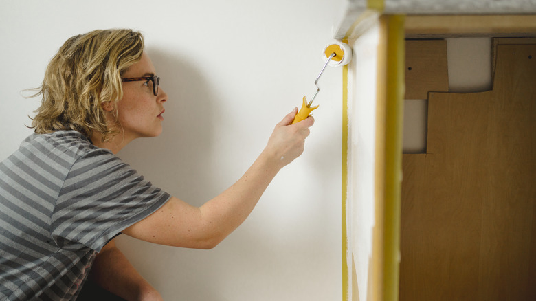 Person painting a wall with a paint roller.