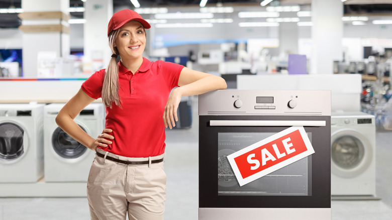 A retail associate stands beside a kitchen appliance labeled with a large "sale" sticker in a store.