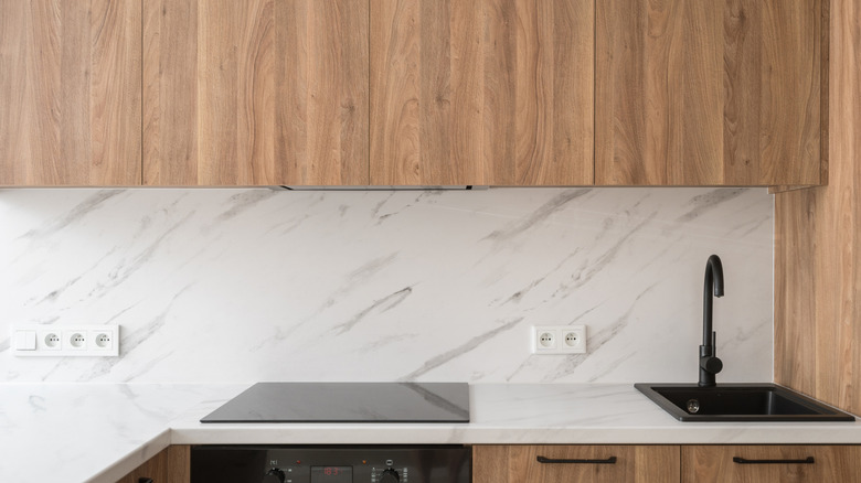 Kitchen cabinets over a marble backsplash, counters, and sink