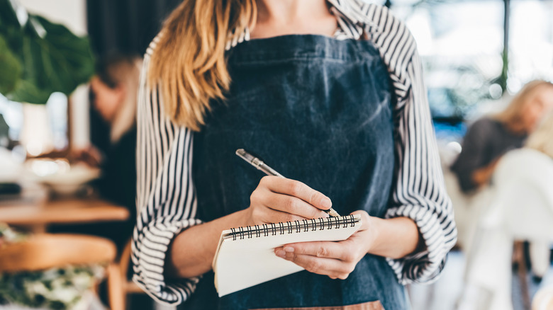 A restaurant server's hands write on a notepad.