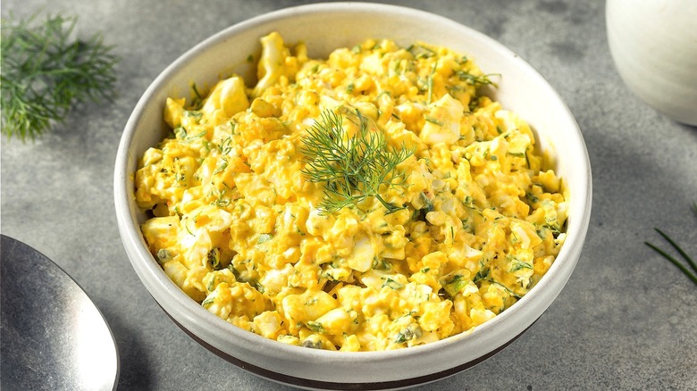 Egg salad with fresh dill in a cream-colored bowl over a gray surface