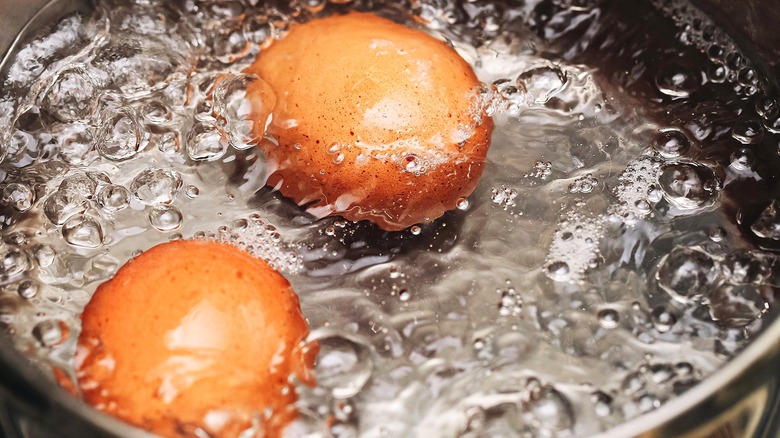 Two whole brown eggs boiling in a steel pot