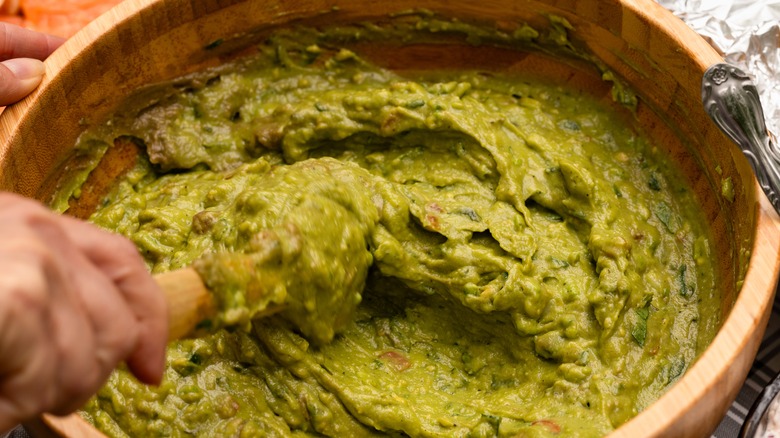 Mixing freshy homemade guacamole in a wooden bowl.