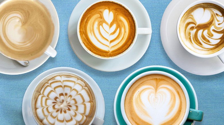 Five lattes with latte art on platters