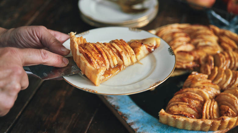 Slice of apple pie being cut from whole pie.