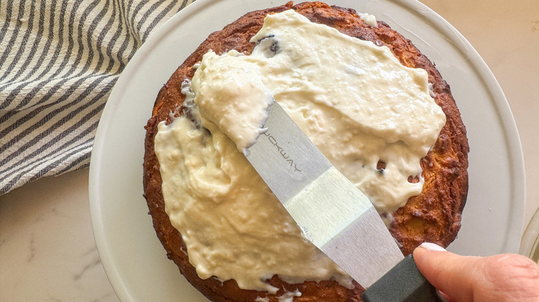 hand spreading frosting on cake