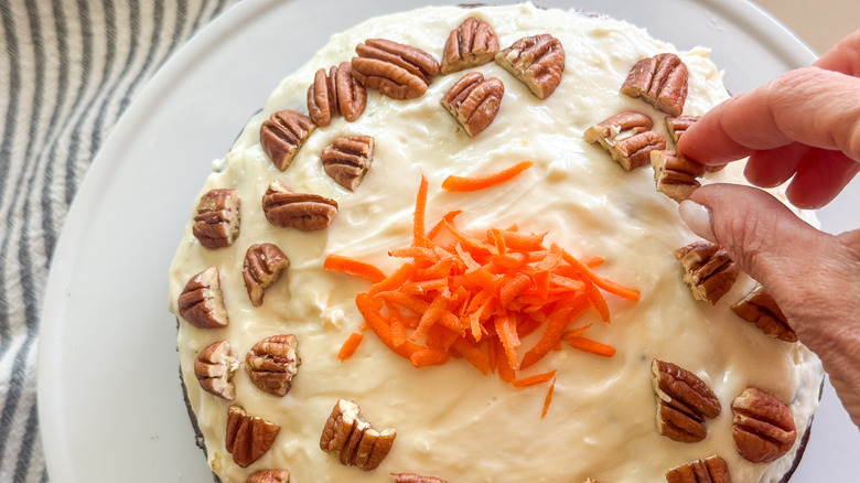 hand adding pecans to carrot cake