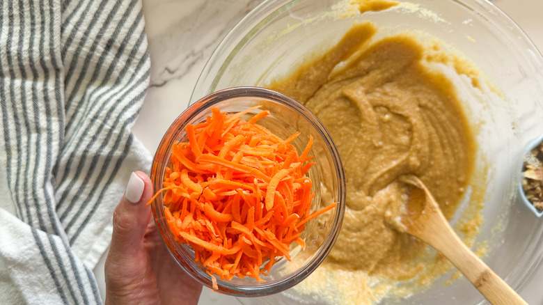 hand adding shredded carrots to bowl with cake batter