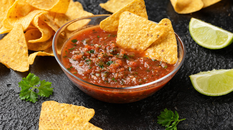 Clear bowl of salsa with tortilla chips and lime slices