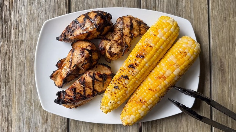 Grilled chicken breasts and corn on the cob on platter with tongs