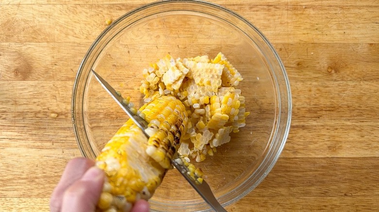 Cutting grilled corn kernels off cob into glass bowl