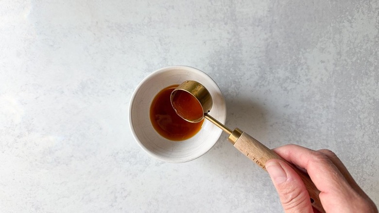 Measuring out tablespoons of chicken marinade into ramekin