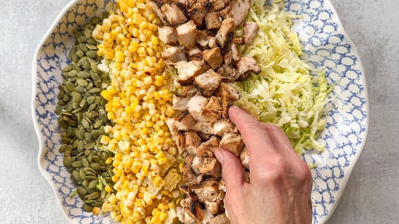 Adding grilled chicken to chopped salad