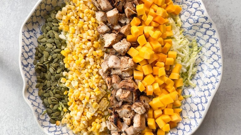 Pepitas, grilled corn, grilled chicken, diced mango, and shredded cabbage in serving bowl