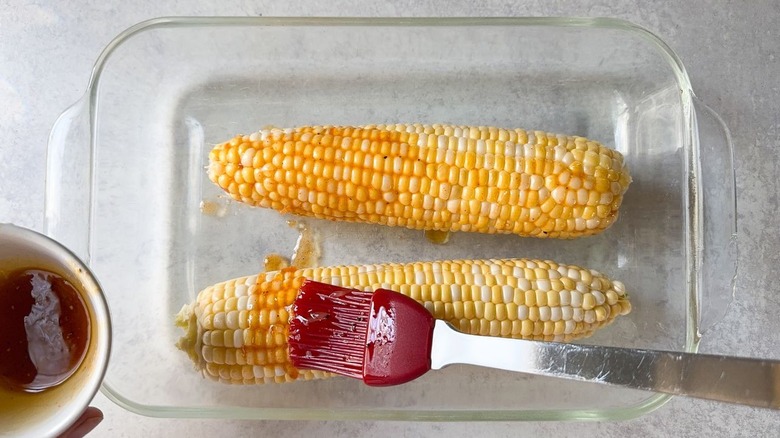Brushing corn on the cob with marinade in glass baking dish