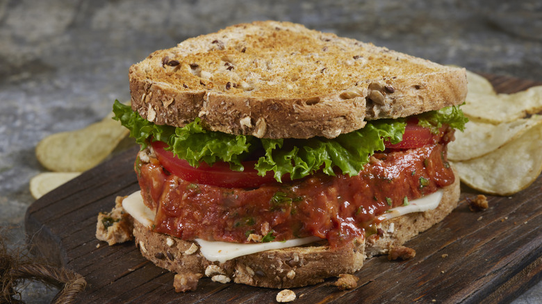 Meatloaf sandwich on toast on a wooden board with chips